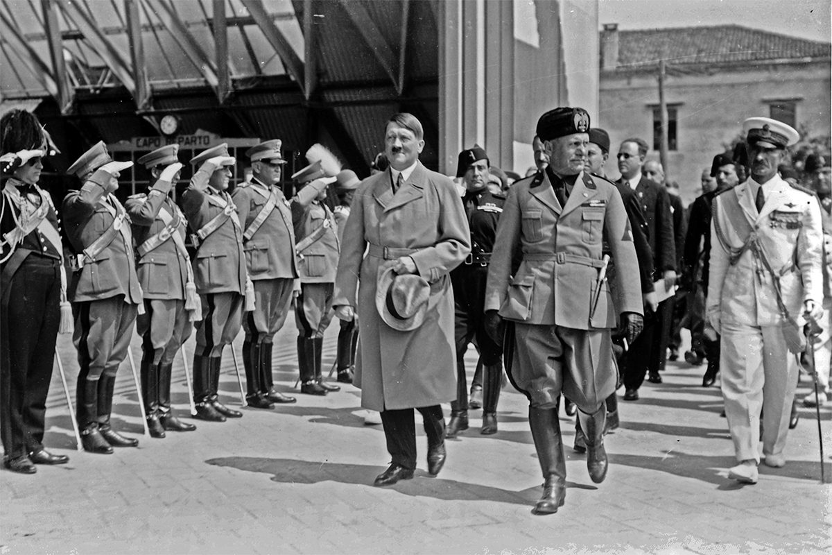 Adolf Hitler and Benito Mussolini walking in front of saluting military during Hitler's visit to Venice, Italy in 1934. // Image from Wikimedia Commons