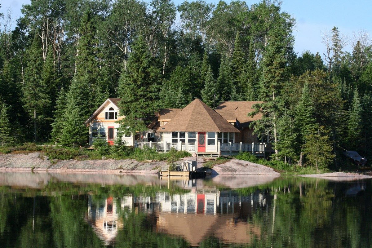 A cbin on teh the lake shore, surrounded by trees