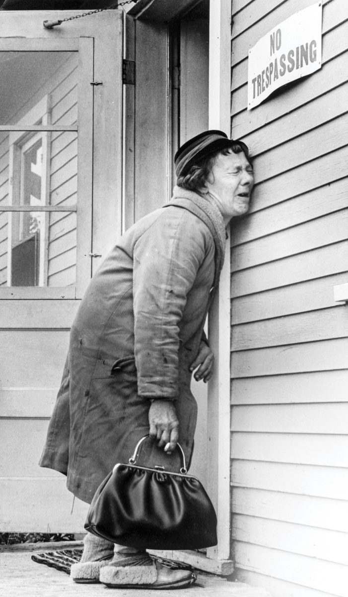 A woman stands sobbing in front of a building in a vintage black-and-white photo.