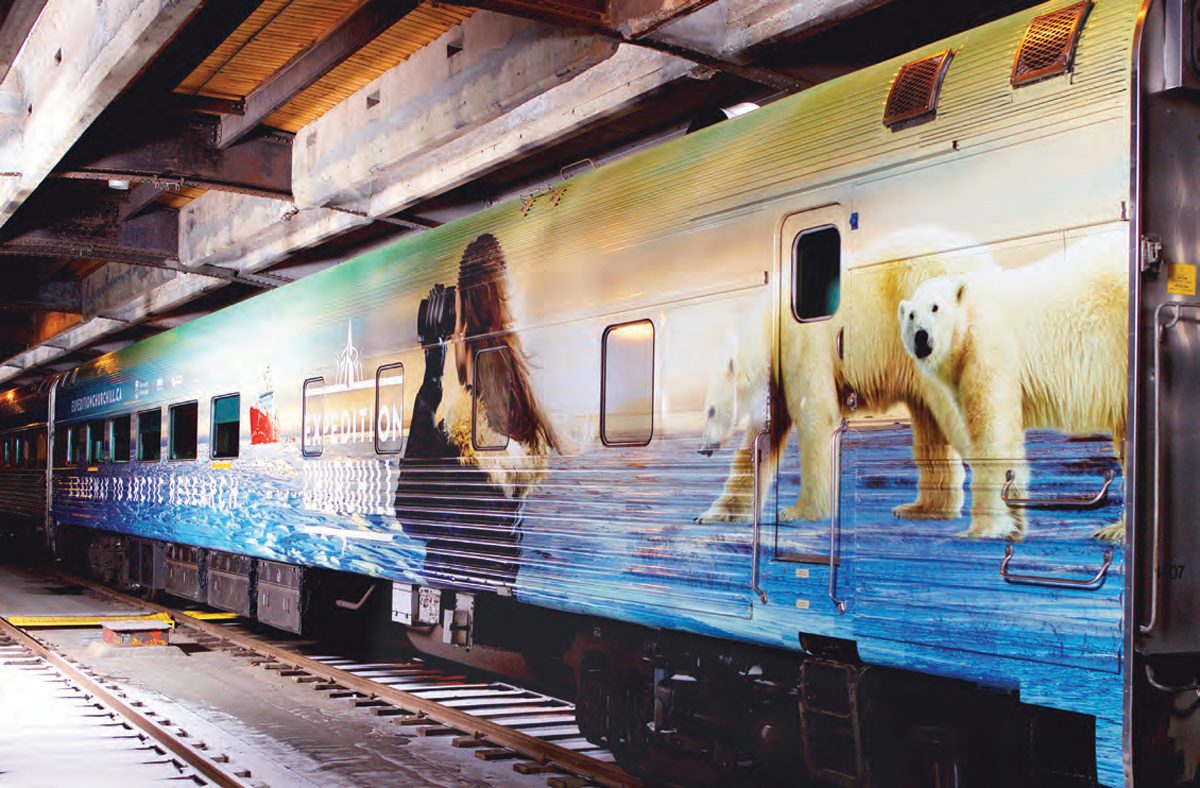 A train car with a colourful Expedition Churchill wrapping showing a polar bear and a woman with binoculars.
