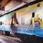 A train car with a colourful Expedition Churchill wrapping showing a polar bear and a woman with binoculars.