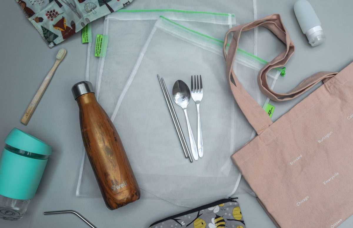 Table with reusable water bottle, cutlery, straw, bag and coffee cup.