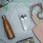 Table with reusable water bottle, cutlery, straw, bag and coffee cup.