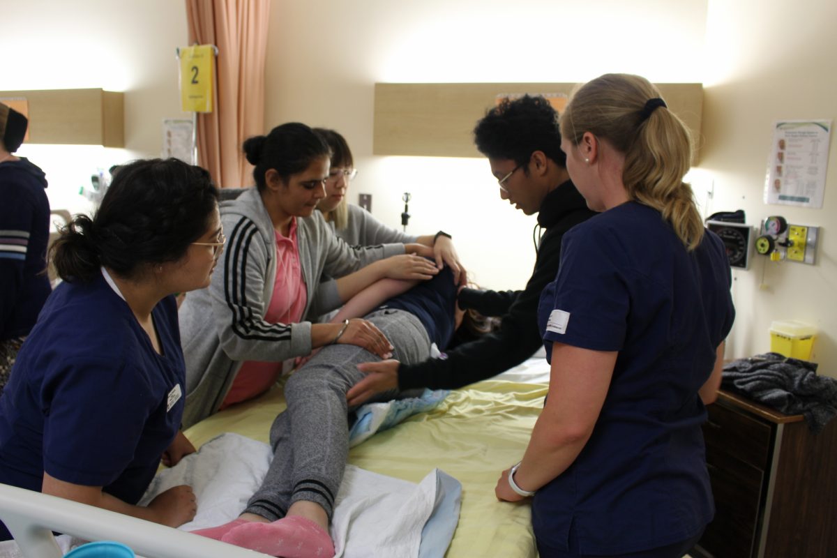 Nursing students practicing skills around a patient's bed