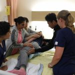 Nursing students practicing skills around a patient's bed