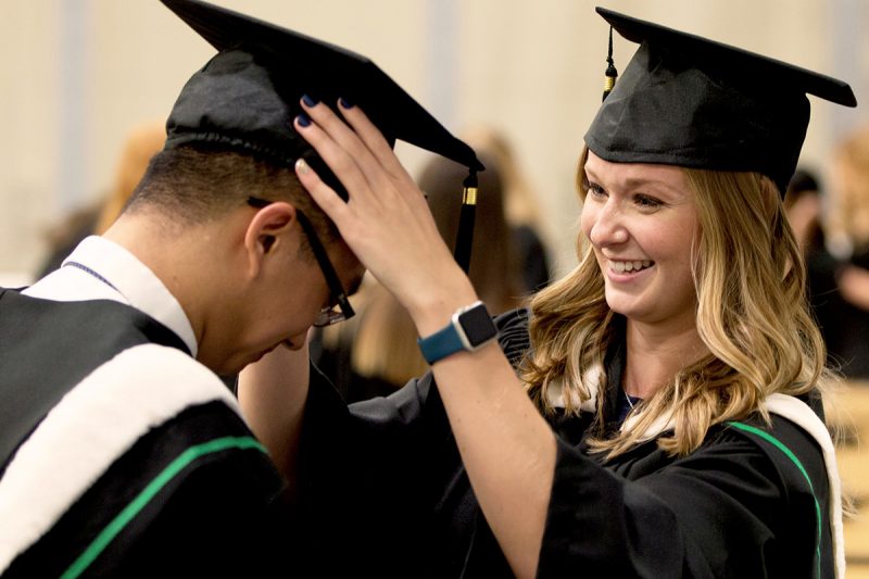 Student helps another student prepare to graduate at Convocation.