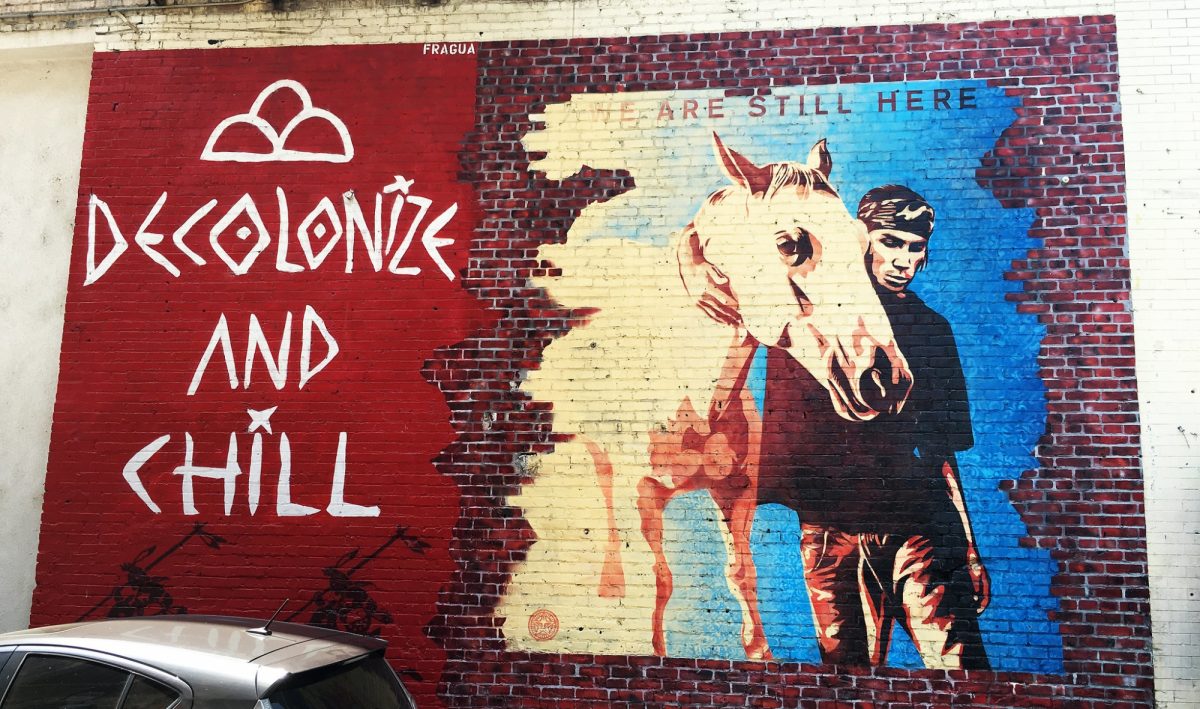 A mural featuring the wordsDecolonize and Chill - We are Still Here, and a man walking a horse