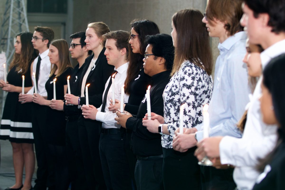 Male and female students wearing black and white hold white candles which are lit.