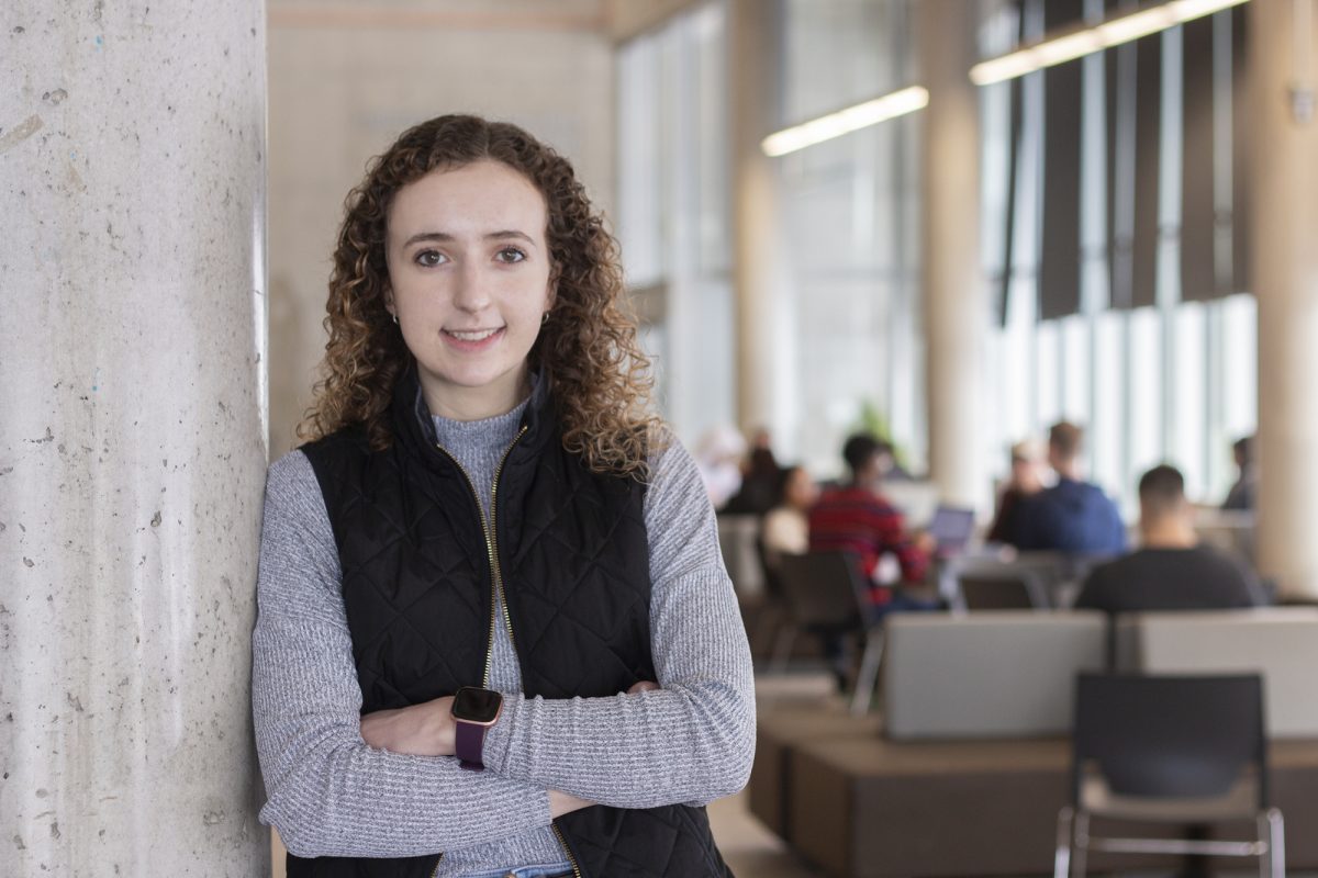 Mackenzie Zacharias in the Active Living Centre agora posing, leaning on a pillar, her arms crossed, smiling.