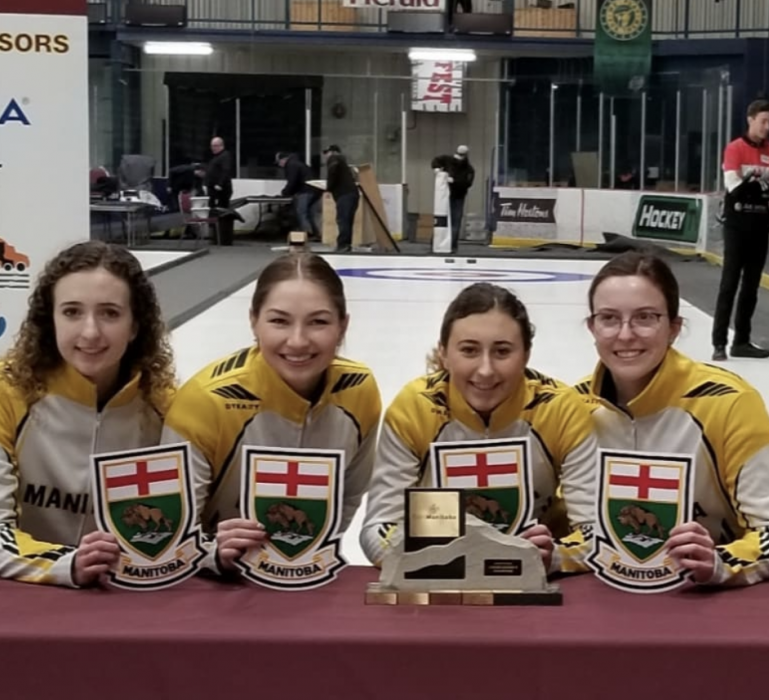Team Manitoba posing with the Canadian junior nationals' trophy and each holding a crest of Manitoba's logo.