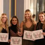 Four young women in formal wear pose for photo smiling, holding certificates and a glass award.