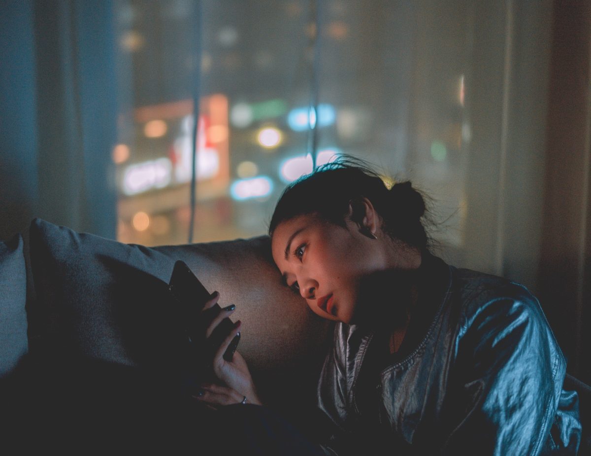 A woman sits on the coach at night, staring at her phone screen