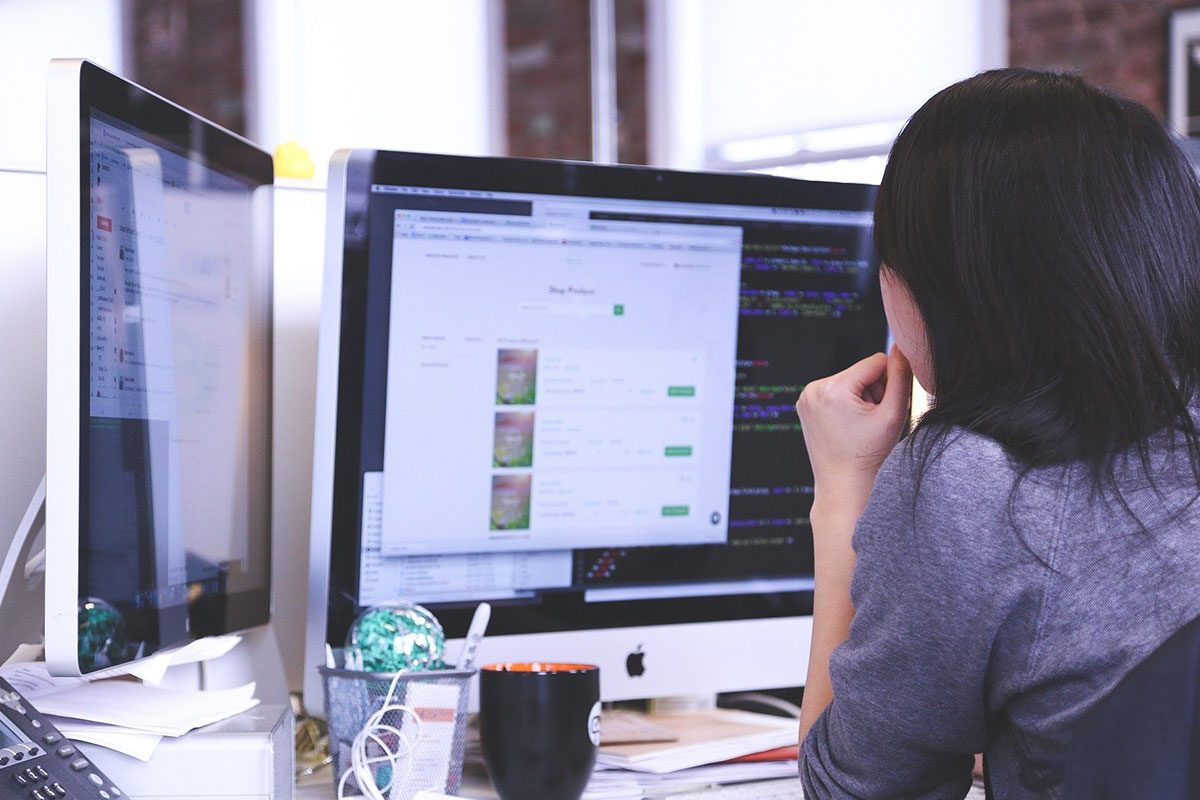 A person works on a computer with two monitor screens.