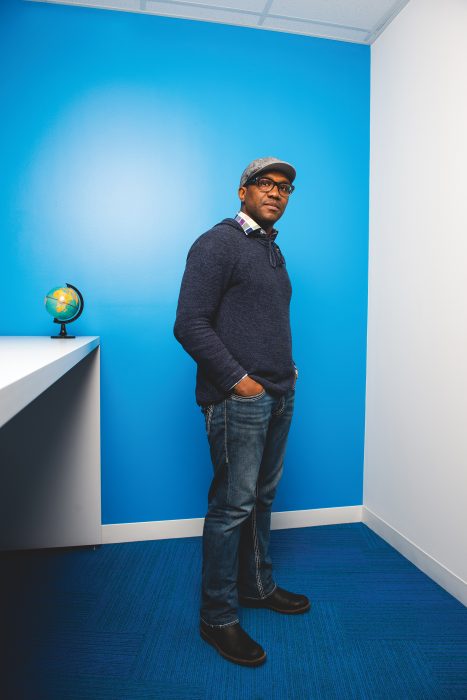Nwora Azubike stands with his hand in his pocket in front of a blue wall.