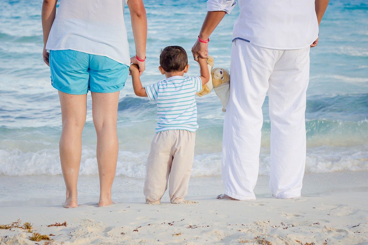 A child with his parents at the beach. // Image from Pixabay