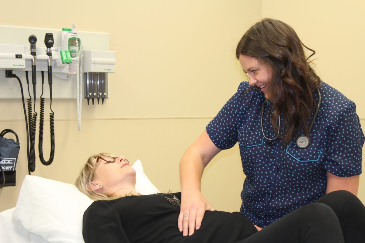 A midwife examines a pregnant woman in a hospital setting.