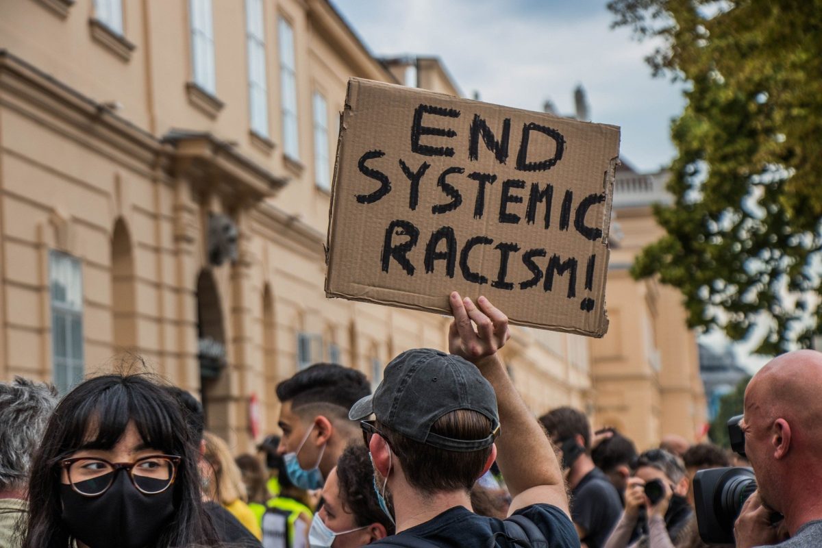 A protestor holds a sign that reads End Systemic Racism
