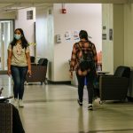 Two students wearing masks walk together down a hallway on campus.