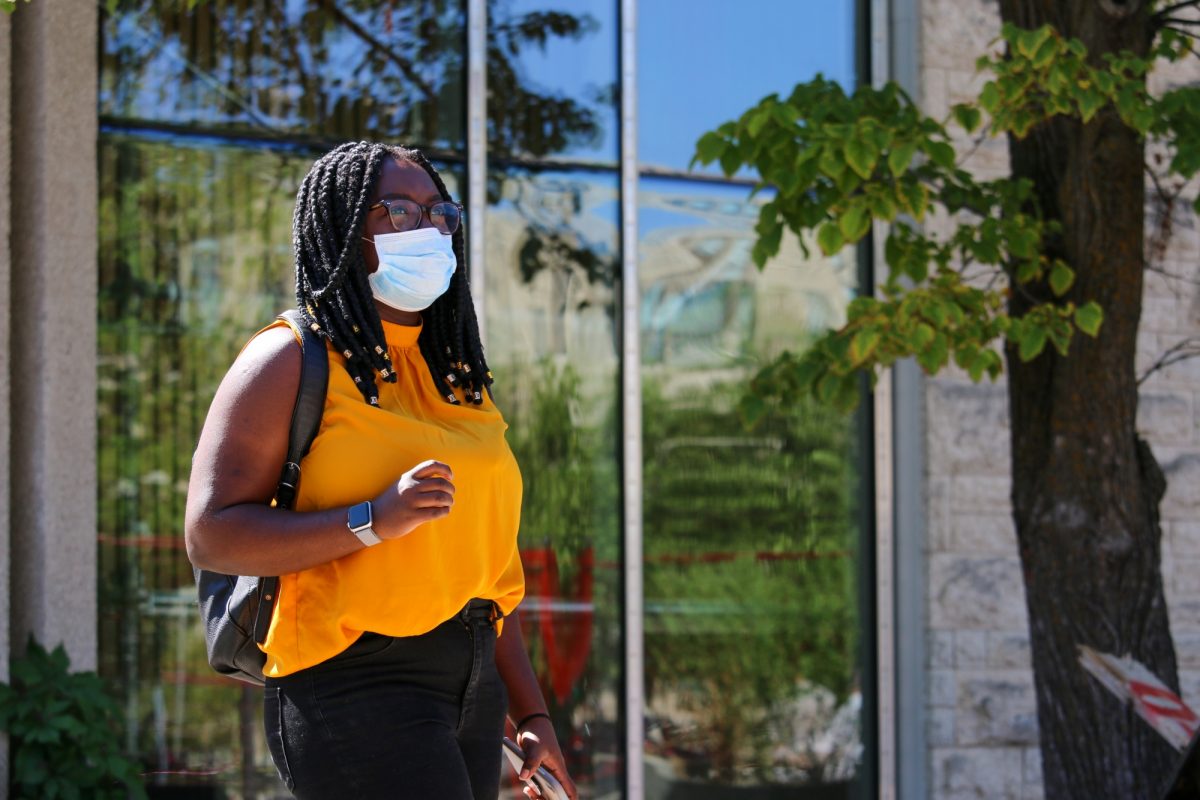 Student wearing mask outdoors on campus with leafy background