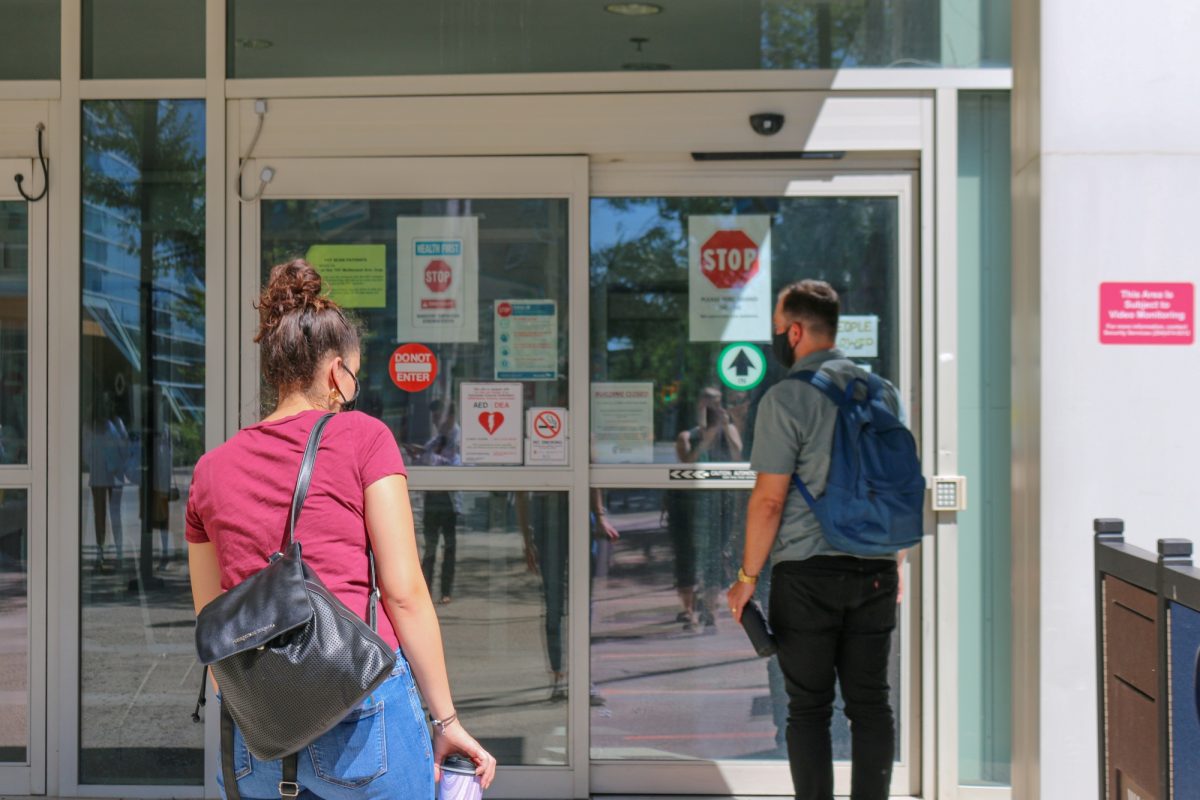 Two people wearing masks are approaching an entrance to Bannatyne campus.