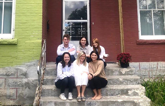 6 students sitting on the front steps of their home