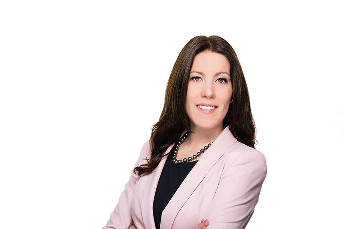 Picture of a woman smiling with her arms crossed. She is wearing a pink blazer and black shirt.