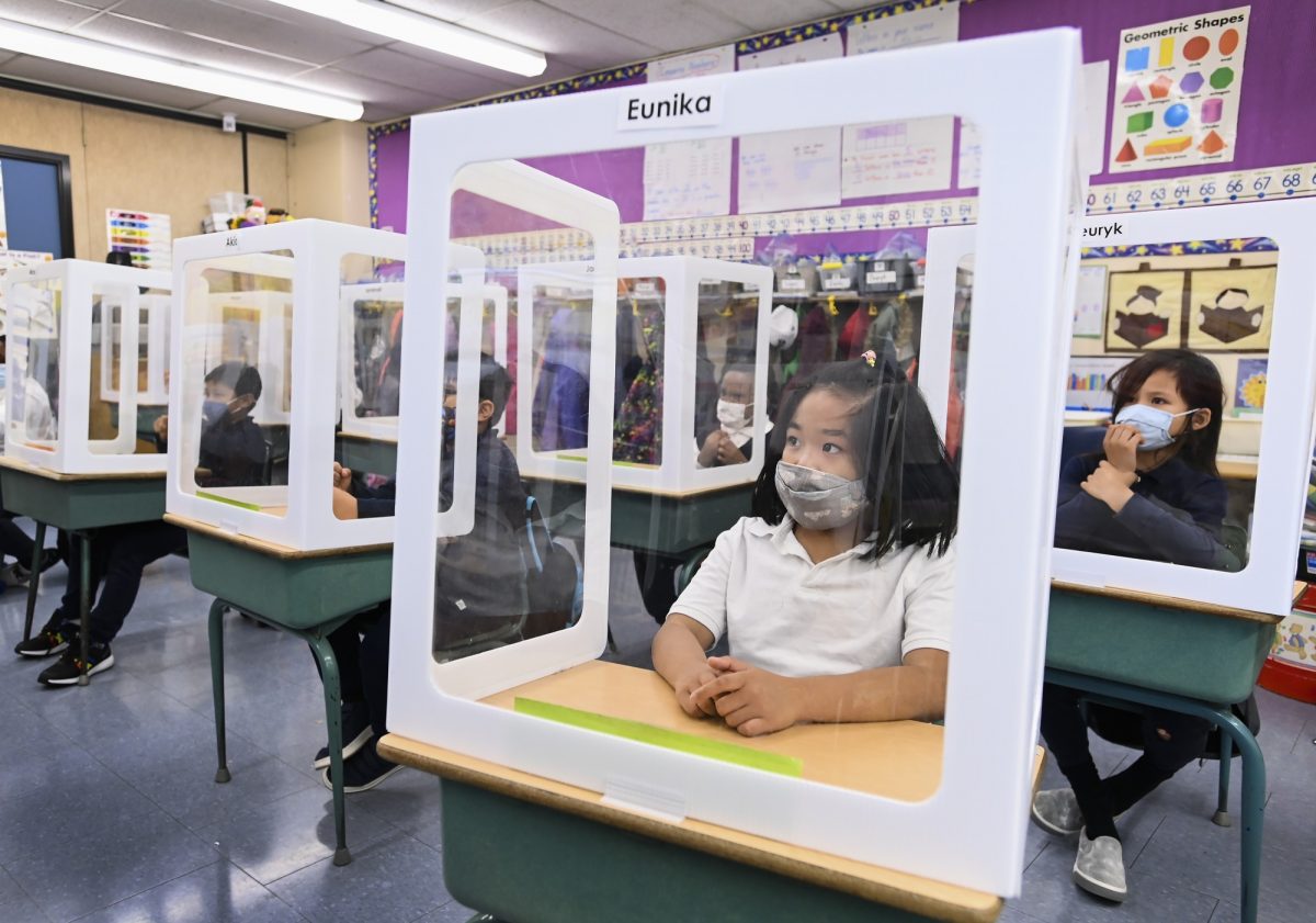 Elementary school students at their desks behind barriers for COVID-19