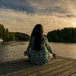 A person meditates on a dock looking towards a lake. // Image from Pixabay