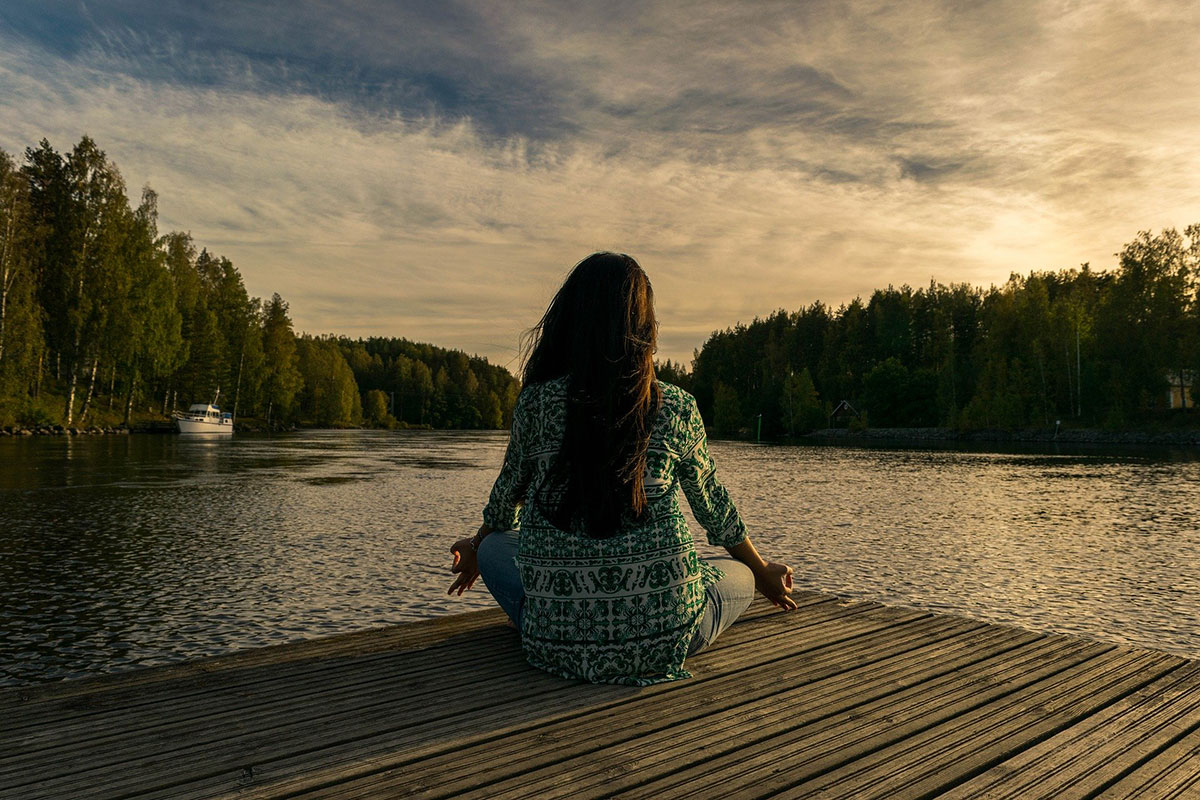 A person meditates on a dock looking towards a lake. // Image from Pixabay