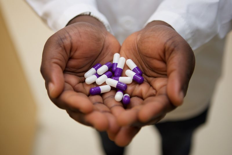 The cupped hands of a person wearing a white lab coat hold medication capsules.