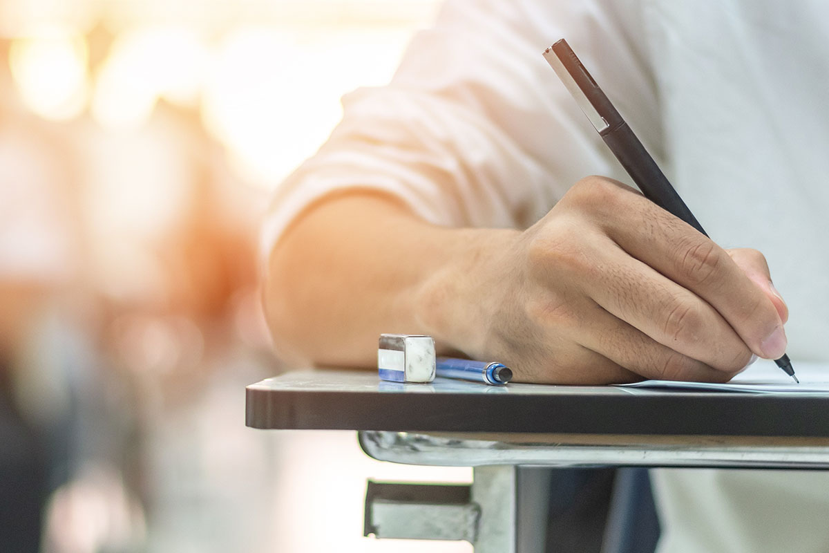 A person sits at a desk, writing on a paper with pen.