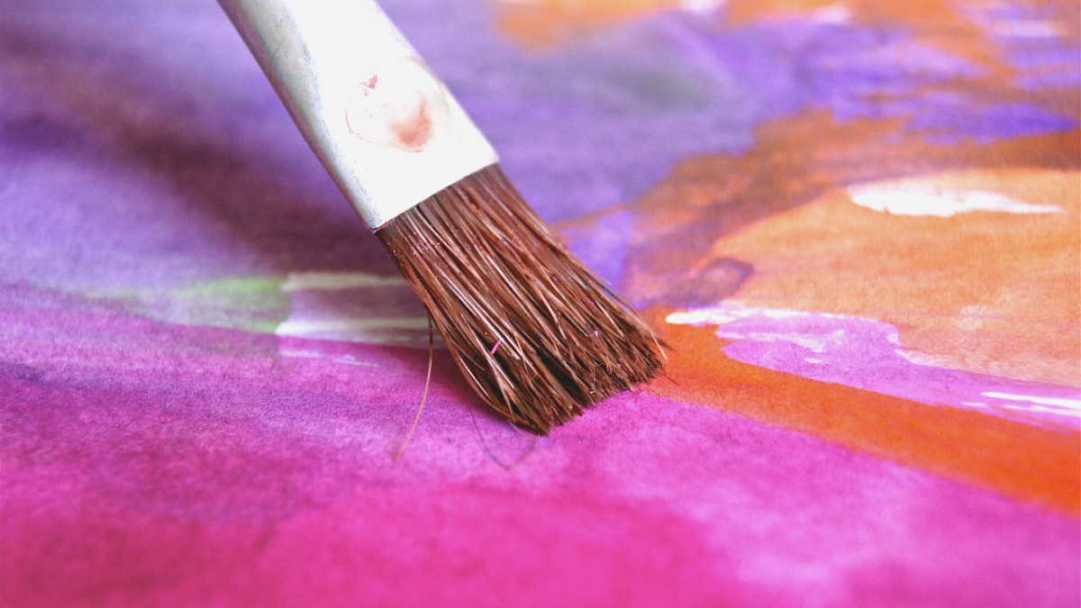 Paintbrush over a colourful background of punk, purple and orange