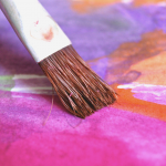 Paintbrush over a colourful background of punk, purple and orange