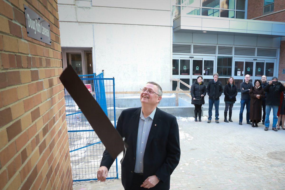 Doug Ruth smiles as he reveals a sign. The sign says "Doug Ruth Laneway"