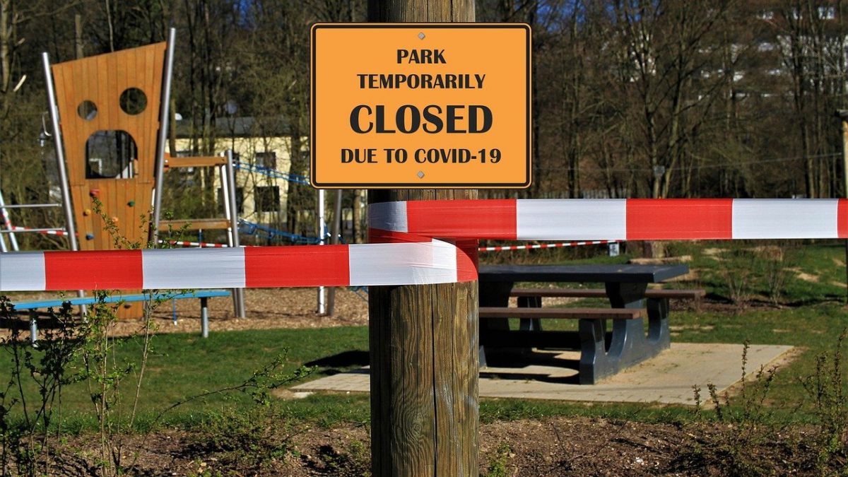 A yellow signs declare a park is closed due to COVID