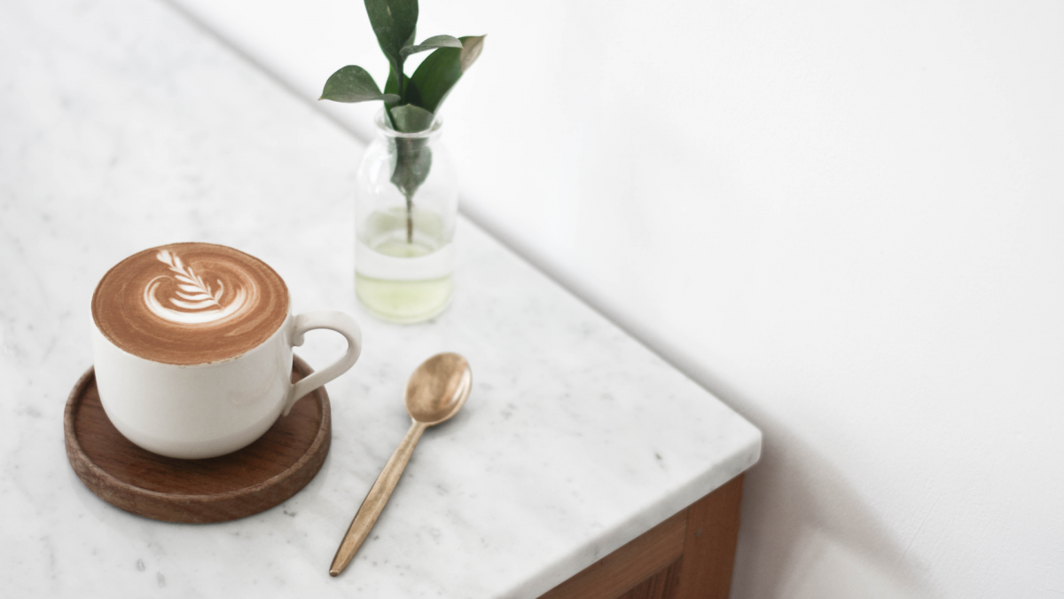 cup of coffee, a stirring spoon, and a small plant on a marble desk