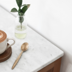 cup of coffee, a stirring spoon, and a small plant on a marble desk