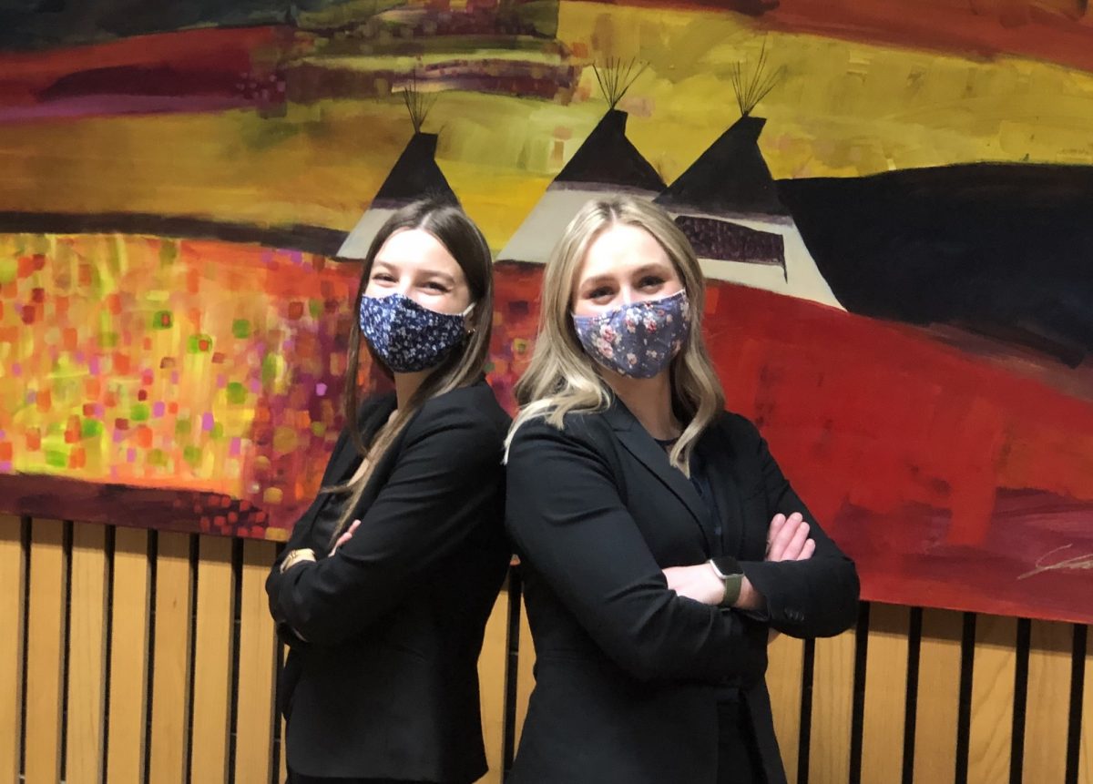 Two law students wearing face masks standing back to back.