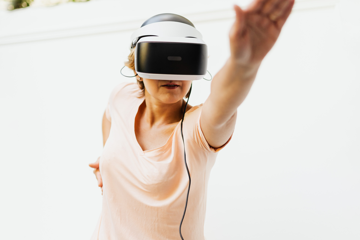 A standing woman wearing a virtual-reality headset stretches one arm upward in front of her.