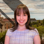 Picture of woman with brown hair and purple shirt smiling. A nice landscape photo of the University of Manitoba in the background.