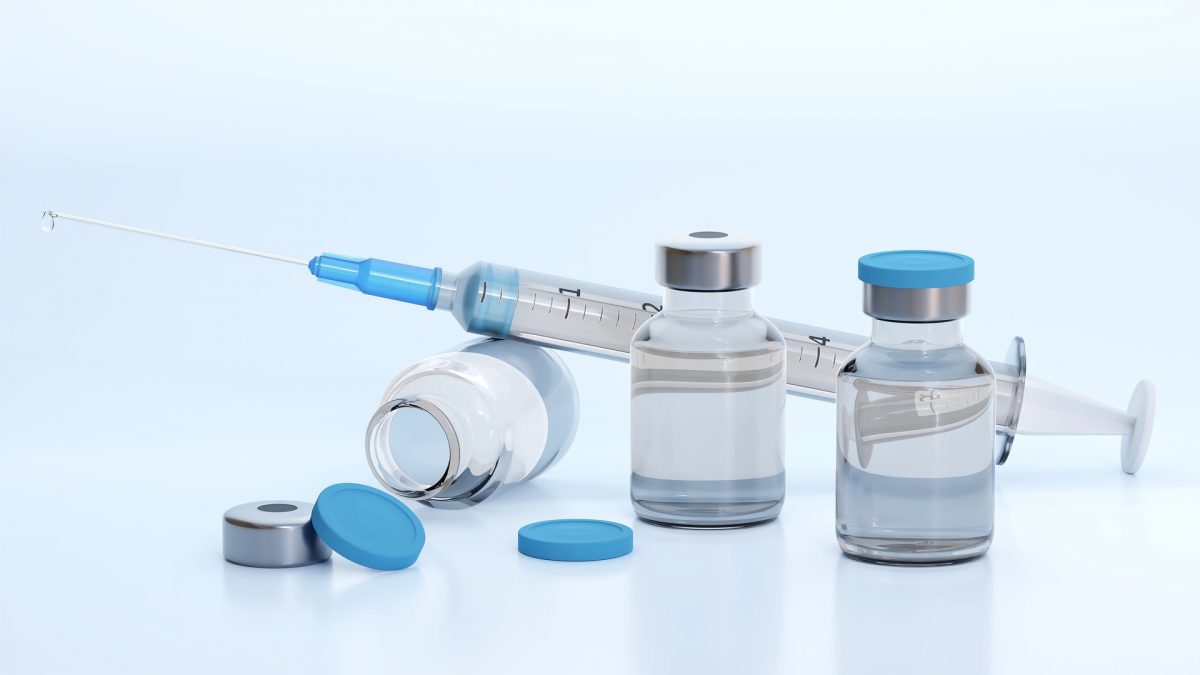 Generic medical syringe leaning on a vial with two upright vials beside it.