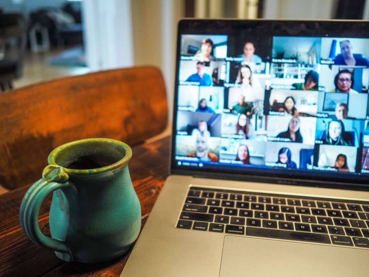 A turquoise and green coffee mug sits beside a laptop with a video chat platform on the screen
