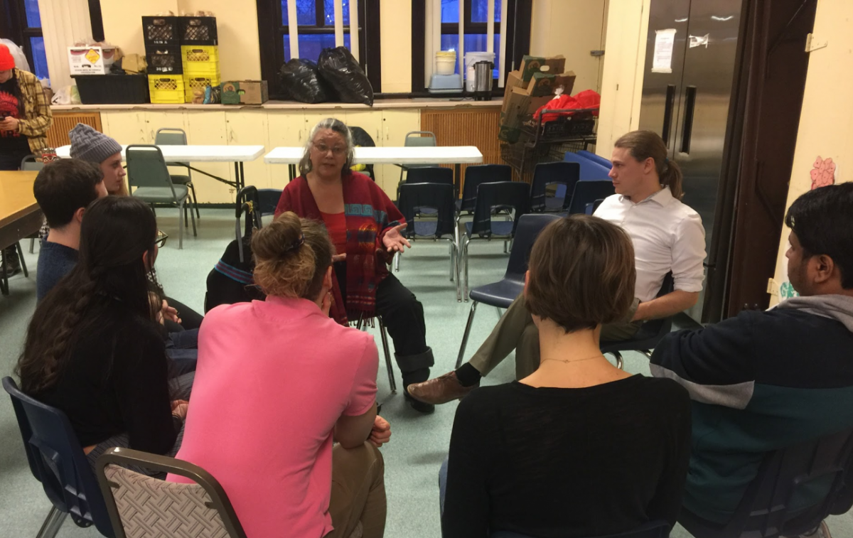 A group of people sitting on chairs in a circle, listening to Audrey Logan speak.