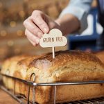 A hand inserts a gluten free sign into a loaf of bread. // Image from Shutterstock