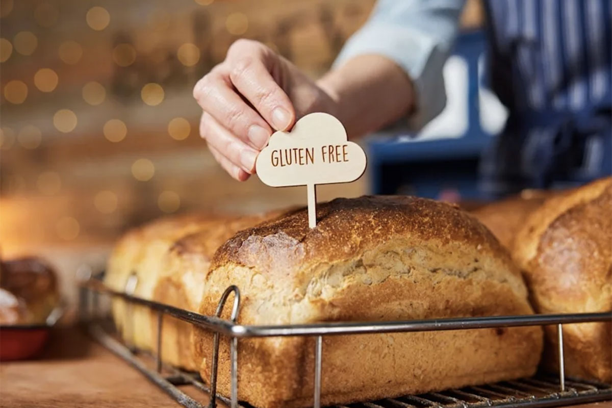 A hand inserts a gluten free sign into a loaf of bread. // Image from Shutterstock