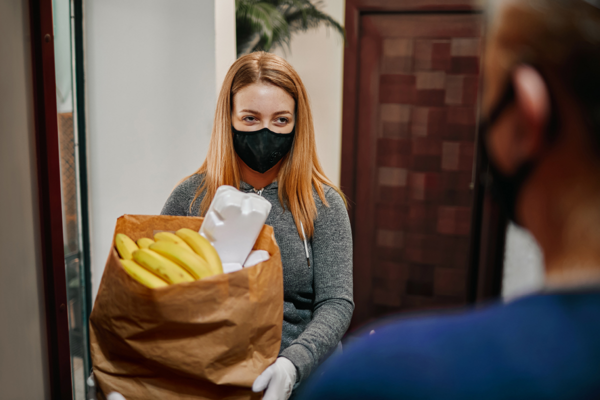 A student with blonde hair wearing a black mask and white disposable gloves accepts a food bank delivery. (Stock photo)