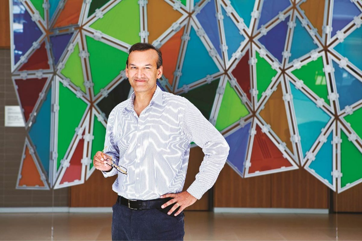 Dr. Prabhat Jha stands in front of a colourful wall decoration.
