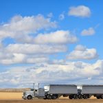 A semi truck drives across the prairie