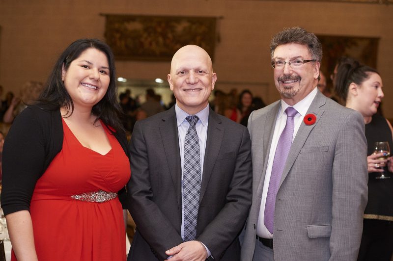 A woman wearing a red dress and two men wearing suits at a business dinner.