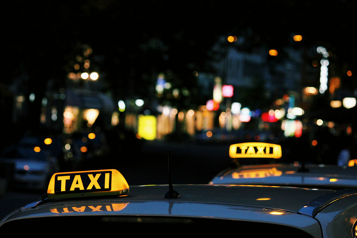 Photo shows yellow taxi lights on roofs of taxis vehicles at night. // Image from Lexi Anderson/Unsplash